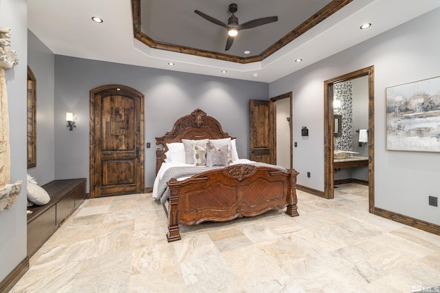 bedroom featuring ceiling fan, connected bathroom, a tray ceiling, and light tile floors