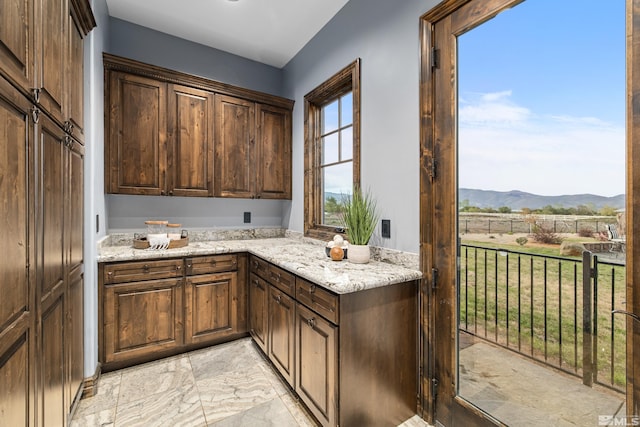 kitchen with light stone counters, a mountain view, light tile floors, and dark brown cabinetry