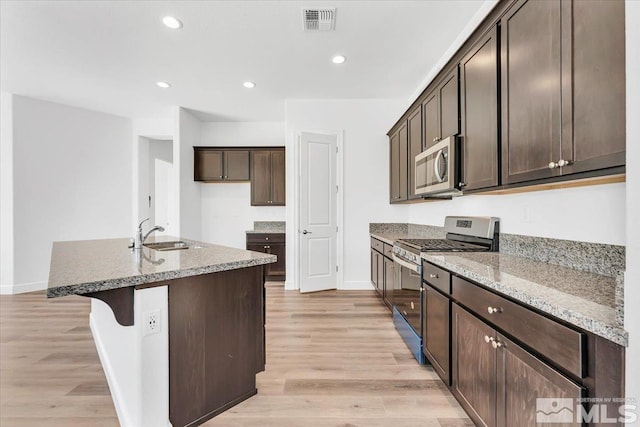 kitchen with a kitchen island with sink, appliances with stainless steel finishes, light wood-type flooring, and sink