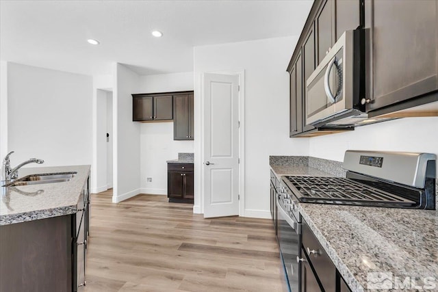 kitchen featuring light wood-type flooring, sink, dark brown cabinets, stainless steel appliances, and light stone countertops