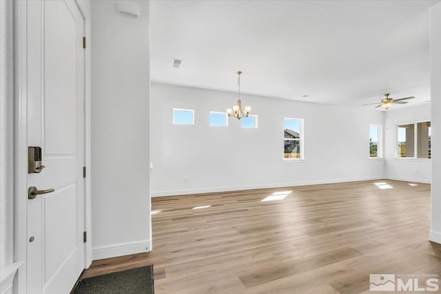 empty room with ceiling fan with notable chandelier and light wood-type flooring