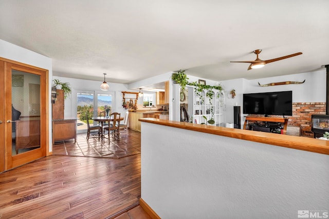 living room with sink, wood-type flooring, ceiling fan, and a wood stove