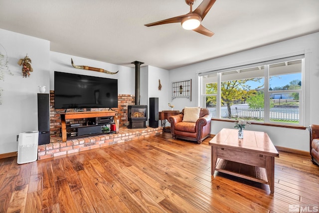 living room with wood-type flooring, ceiling fan, and a wood stove