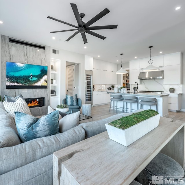 living room featuring a premium fireplace, built in features, ceiling fan, and light hardwood / wood-style flooring