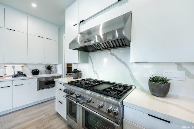 kitchen with appliances with stainless steel finishes, white cabinetry, wall chimney exhaust hood, and light hardwood / wood-style floors