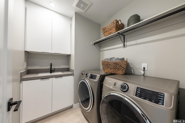 clothes washing area featuring cabinets, sink, light wood-type flooring, and washing machine and clothes dryer