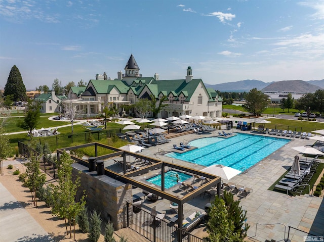 view of pool featuring a hot tub, a patio, a lawn, and a mountain view