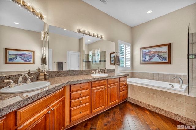 bathroom featuring a relaxing tiled bath, dual sinks, oversized vanity, and wood-type flooring