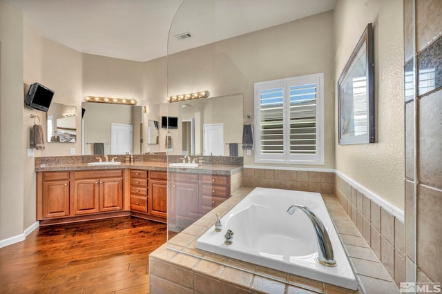 bathroom featuring double vanity, tiled tub, and hardwood / wood-style floors