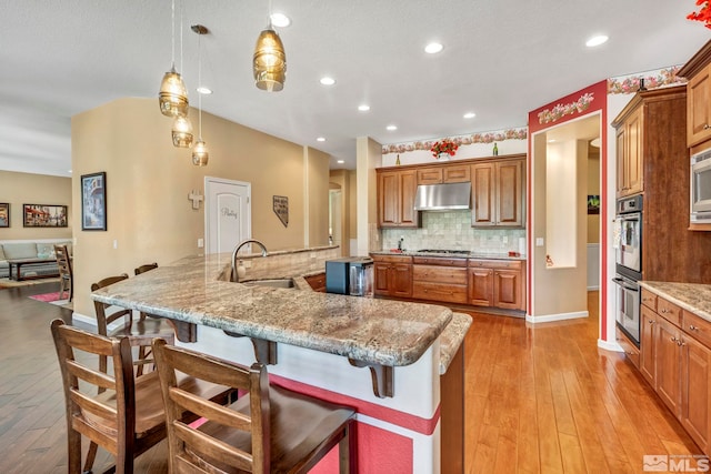 kitchen with a breakfast bar area, light hardwood / wood-style floors, backsplash, and appliances with stainless steel finishes