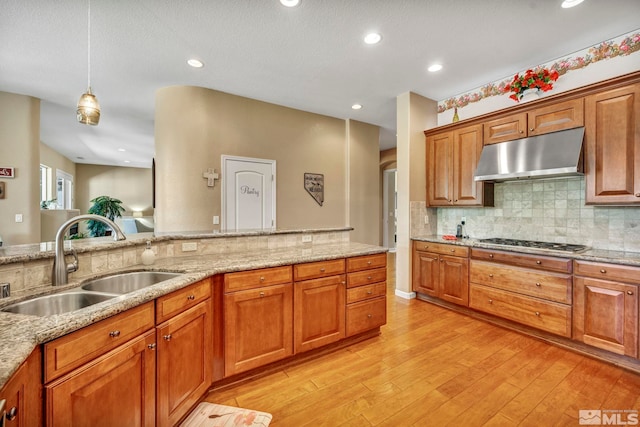 kitchen featuring hanging light fixtures, sink, stainless steel gas stovetop, and light hardwood / wood-style flooring