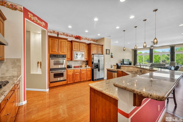 kitchen featuring appliances with stainless steel finishes, sink, tasteful backsplash, and light hardwood / wood-style flooring