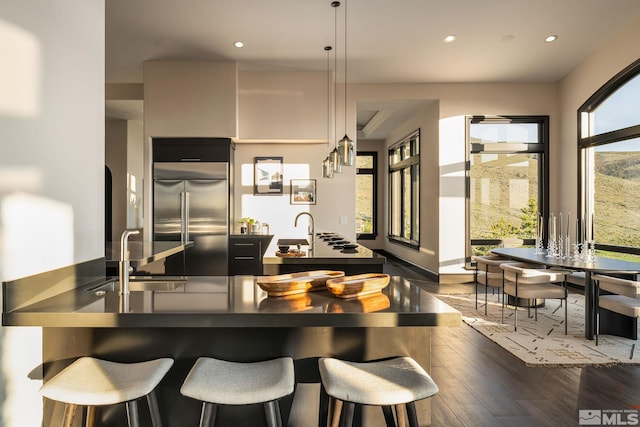 kitchen with built in fridge, dark wood-type flooring, white cabinets, sink, and pendant lighting