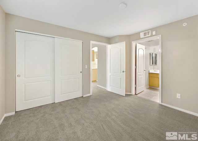 unfurnished bedroom with light colored carpet, a closet, and ensuite bath