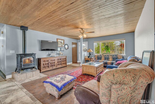 living room featuring tile floors, ceiling fan, a wood stove, and wood ceiling