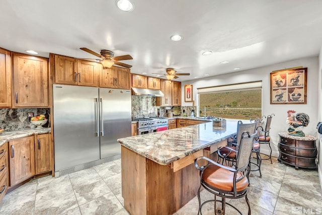 kitchen with light tile floors, high quality appliances, ceiling fan, and light stone counters