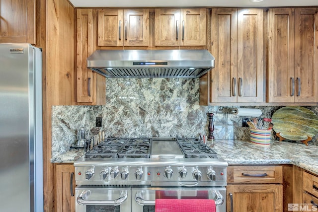 kitchen with stainless steel appliances, light stone counters, wall chimney exhaust hood, and tasteful backsplash