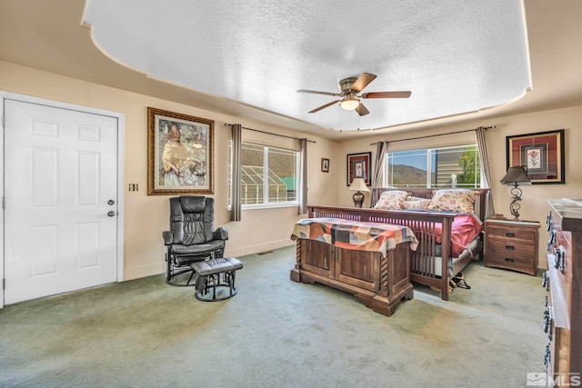 carpeted bedroom with a textured ceiling, ceiling fan, and a tray ceiling