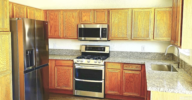 kitchen with stainless steel appliances, dark wood-type flooring, sink, and light stone counters