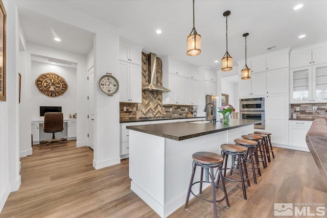 kitchen with white cabinetry, light hardwood / wood-style flooring, wall chimney exhaust hood, and stainless steel appliances