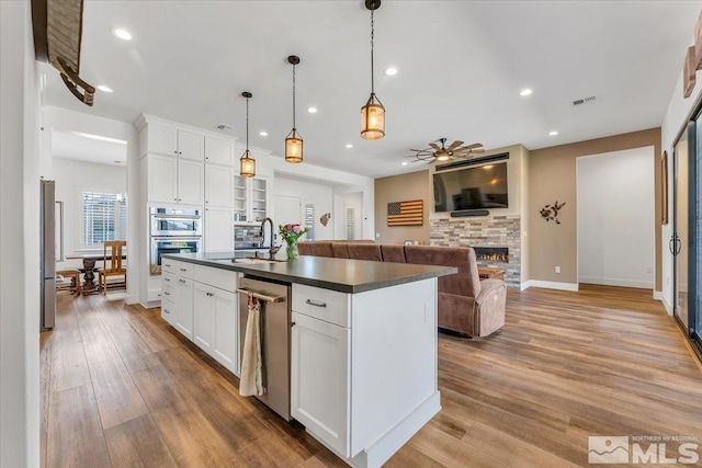 kitchen with light wood-type flooring, sink, a center island with sink, a fireplace, and white cabinetry