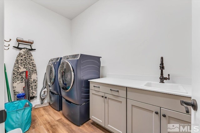 laundry room featuring washing machine and clothes dryer, light hardwood / wood-style floors, cabinets, and sink