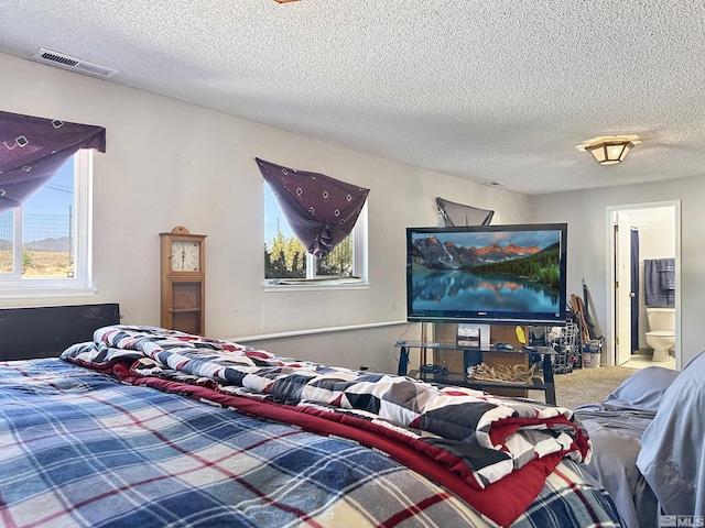 carpeted bedroom with a textured ceiling and ensuite bath