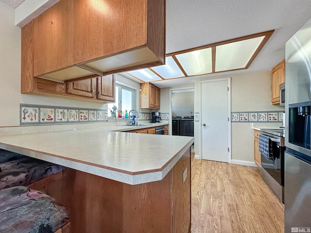 kitchen with sink, light wood-type flooring, appliances with stainless steel finishes, kitchen peninsula, and washing machine and clothes dryer