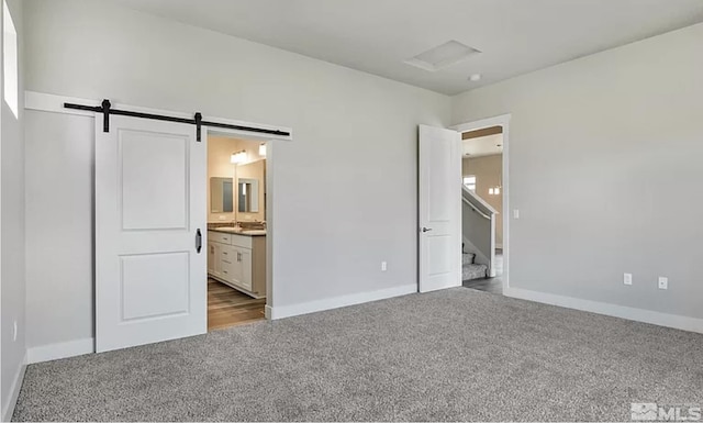 unfurnished bedroom with a barn door, light colored carpet, and connected bathroom