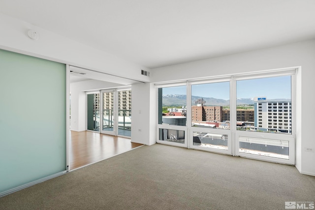 carpeted empty room with a view of city, visible vents, and a mountain view