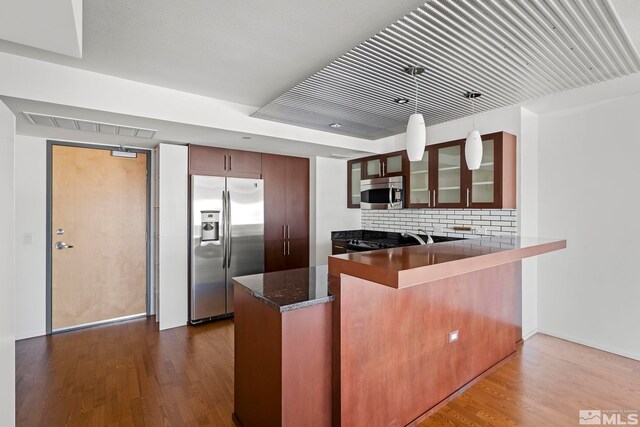 kitchen featuring stainless steel appliances, kitchen peninsula, hardwood / wood-style flooring, and tasteful backsplash