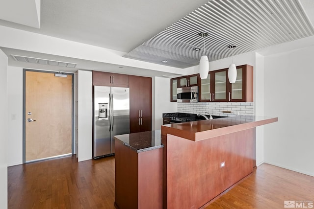 kitchen with visible vents, glass insert cabinets, appliances with stainless steel finishes, a peninsula, and dark wood-style flooring