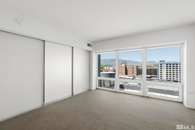 carpeted empty room featuring visible vents, a view of city, and a mountain view