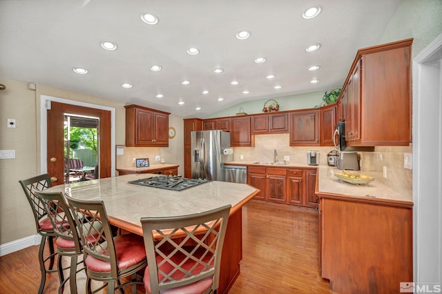 kitchen with decorative backsplash, appliances with stainless steel finishes, sink, light hardwood / wood-style flooring, and a center island