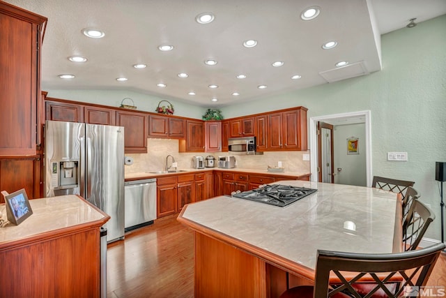 kitchen with sink, a center island, lofted ceiling, a breakfast bar, and appliances with stainless steel finishes