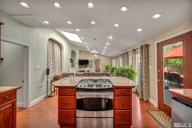 kitchen featuring appliances with stainless steel finishes, vaulted ceiling with skylight, a center island, light hardwood / wood-style floors, and hanging light fixtures