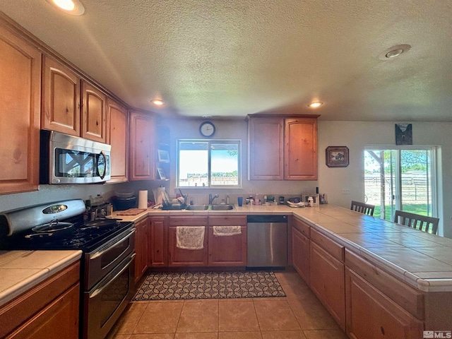 kitchen with stainless steel appliances, tile counters, sink, and light tile floors