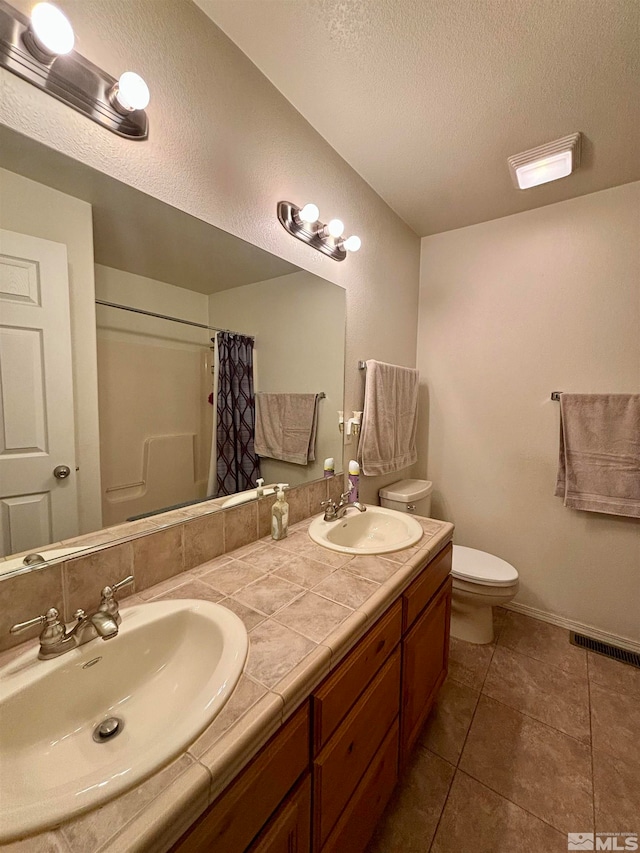 bathroom with tile floors, a textured ceiling, double vanity, and toilet