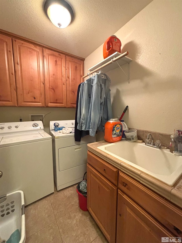 laundry area with washing machine and dryer, a textured ceiling, light tile floors, sink, and cabinets