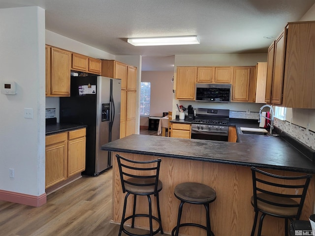 kitchen with a kitchen bar, sink, wood-type flooring, kitchen peninsula, and stainless steel appliances