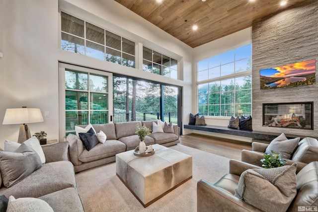 living room with a fireplace, a towering ceiling, wood ceiling, and light wood-type flooring