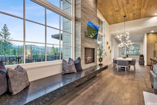 living room with a towering ceiling, wood ceiling, a large fireplace, dark wood-type flooring, and a chandelier