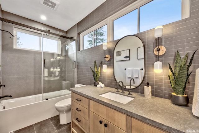 full bathroom featuring tile patterned flooring, toilet, shower / bath combination with glass door, vanity, and tile walls