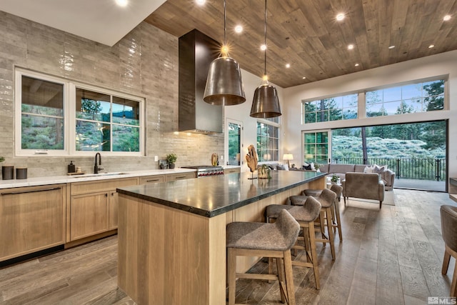 kitchen featuring sink, hanging light fixtures, a high ceiling, wall chimney range hood, and a kitchen island