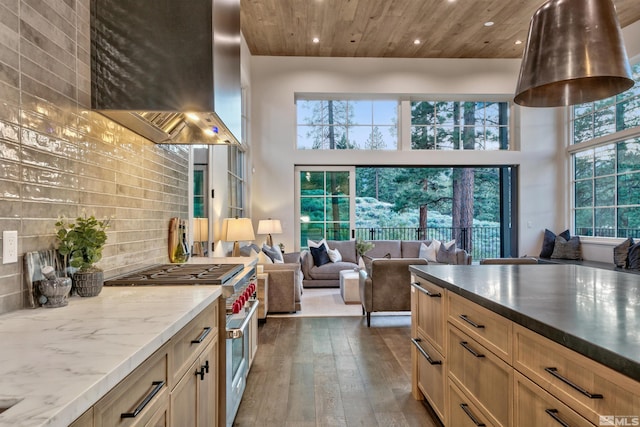 kitchen featuring light brown cabinetry, high end stainless steel range oven, dark wood-type flooring, wall chimney range hood, and a high ceiling