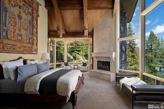 carpeted bedroom with beamed ceiling, a tile fireplace, a high ceiling, and multiple windows