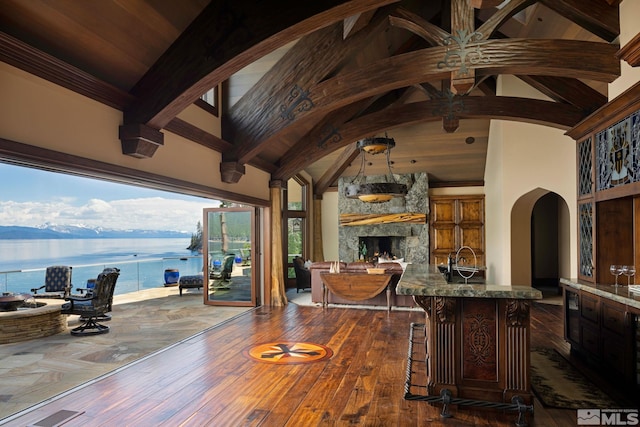 dining space featuring a stone fireplace, a water view, high vaulted ceiling, dark hardwood / wood-style flooring, and beam ceiling