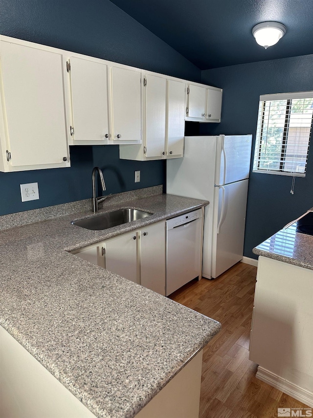 kitchen with white appliances, kitchen peninsula, light stone countertops, white cabinets, and sink