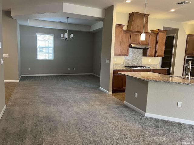 kitchen with pendant lighting, dark colored carpet, sink, light stone countertops, and tasteful backsplash