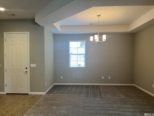 spare room with a tray ceiling and an inviting chandelier